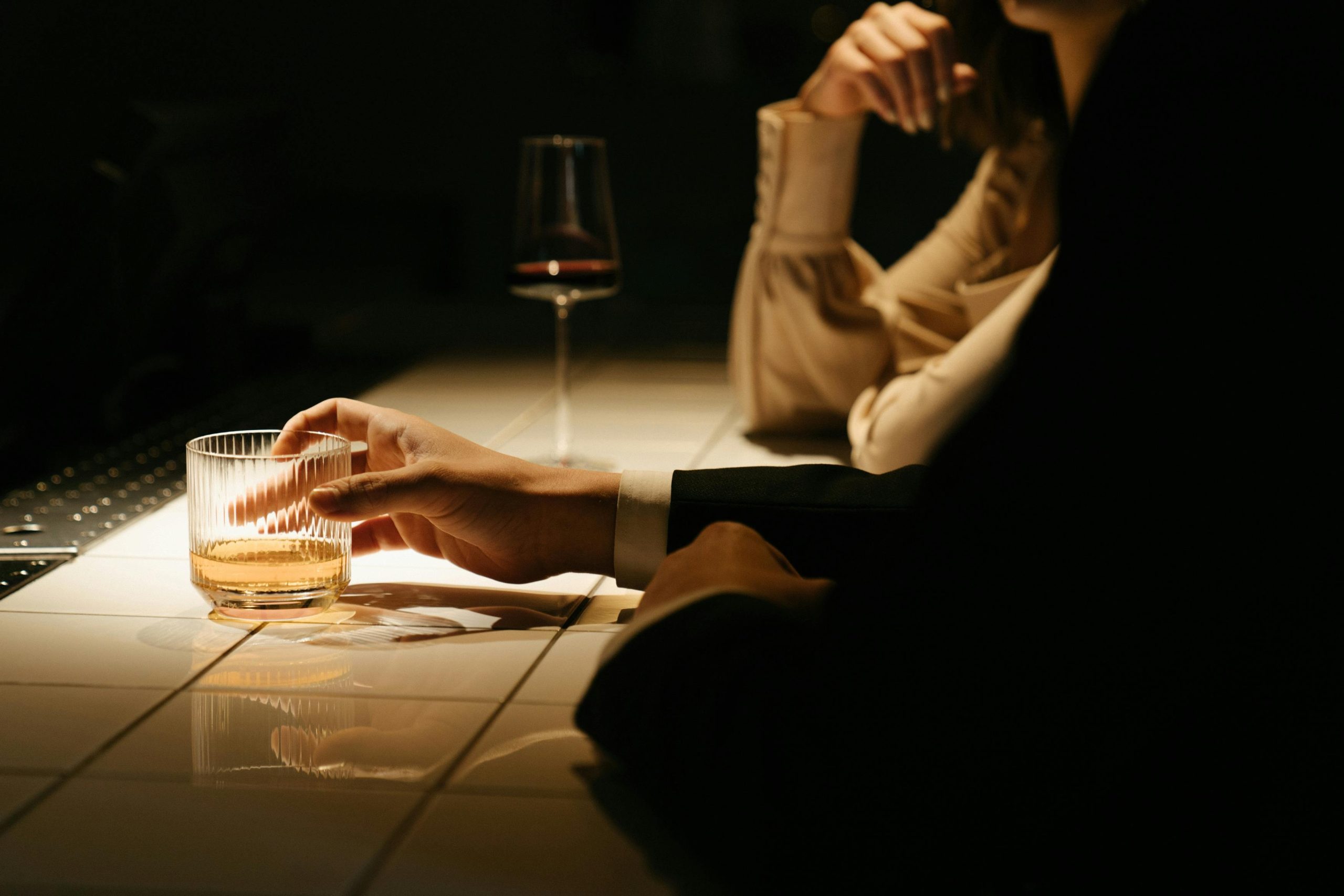 Man holding glass of alcohol in dark symbolizing alcohol addiction and recovery.